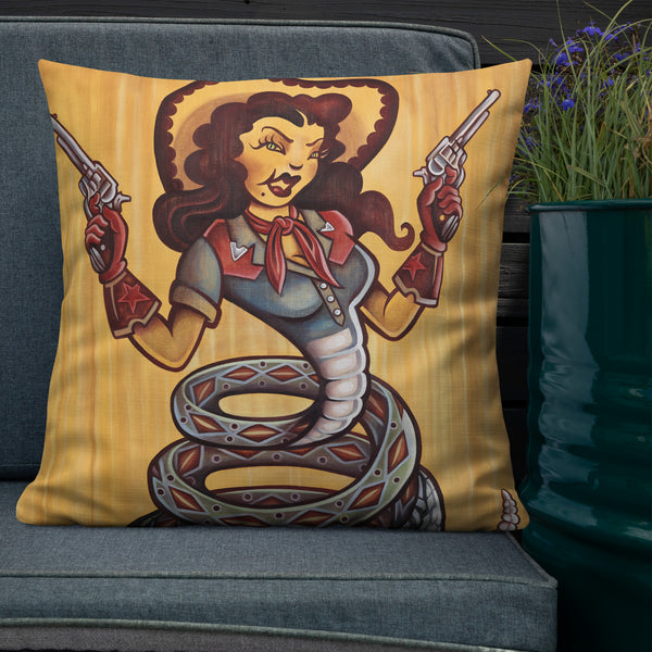 Cowgirl Pillow - Choice Goods Gallery. Cowgirl with six shooters wearing red gloves and cowboy hat, western shirt with a red bandana. She has a snake body with a rattlesnake tail. Green snake eyes and dark hair, on a gold yellow background, shows pillow on a sofa outdoors