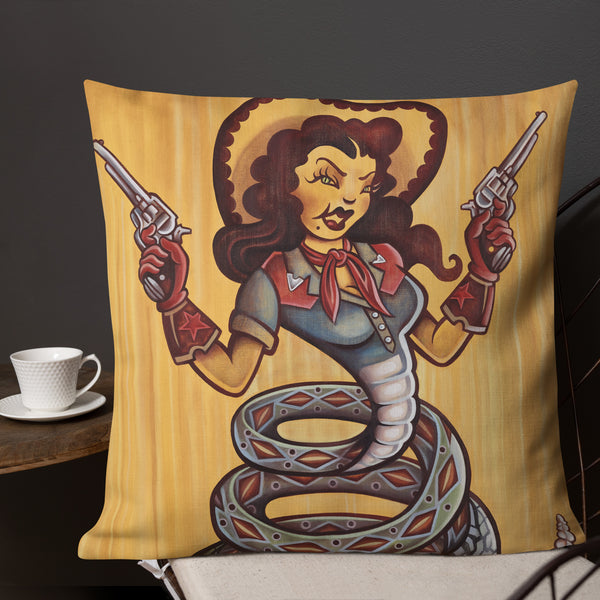 Cowgirl Pillow - Choice Goods Gallery. Cowgirl with six shooters wearing red gloves and cowboy hat, western shirt with a red bandana. She has a snake body with a rattlesnake tail. Green snake eyes and dark hair, on a gold yellow background. shows image of pillow in a livingroom setting.